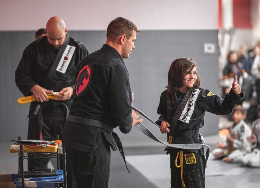 A parent’s trust improves progress in martial arts training Martial arts instructor awarding a kid with his new belt