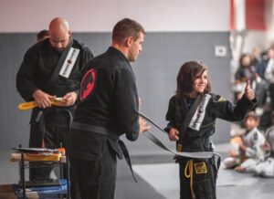 A parent’s trust improves progress in martial arts training Martial arts instructor awarding a kid with his new belt