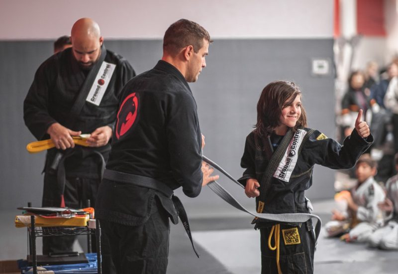 A parent’s trust improves progress in martial arts training Martial arts instructor awarding a kid with his new belt